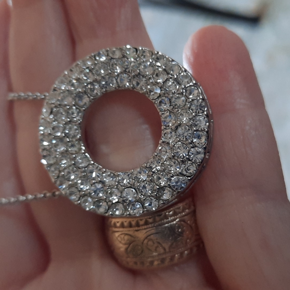 Circular clear stone pendant on silver tone chain